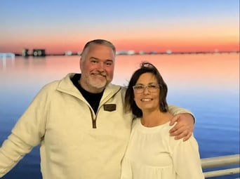 A smiling man and woman standing together with a scenic sunset